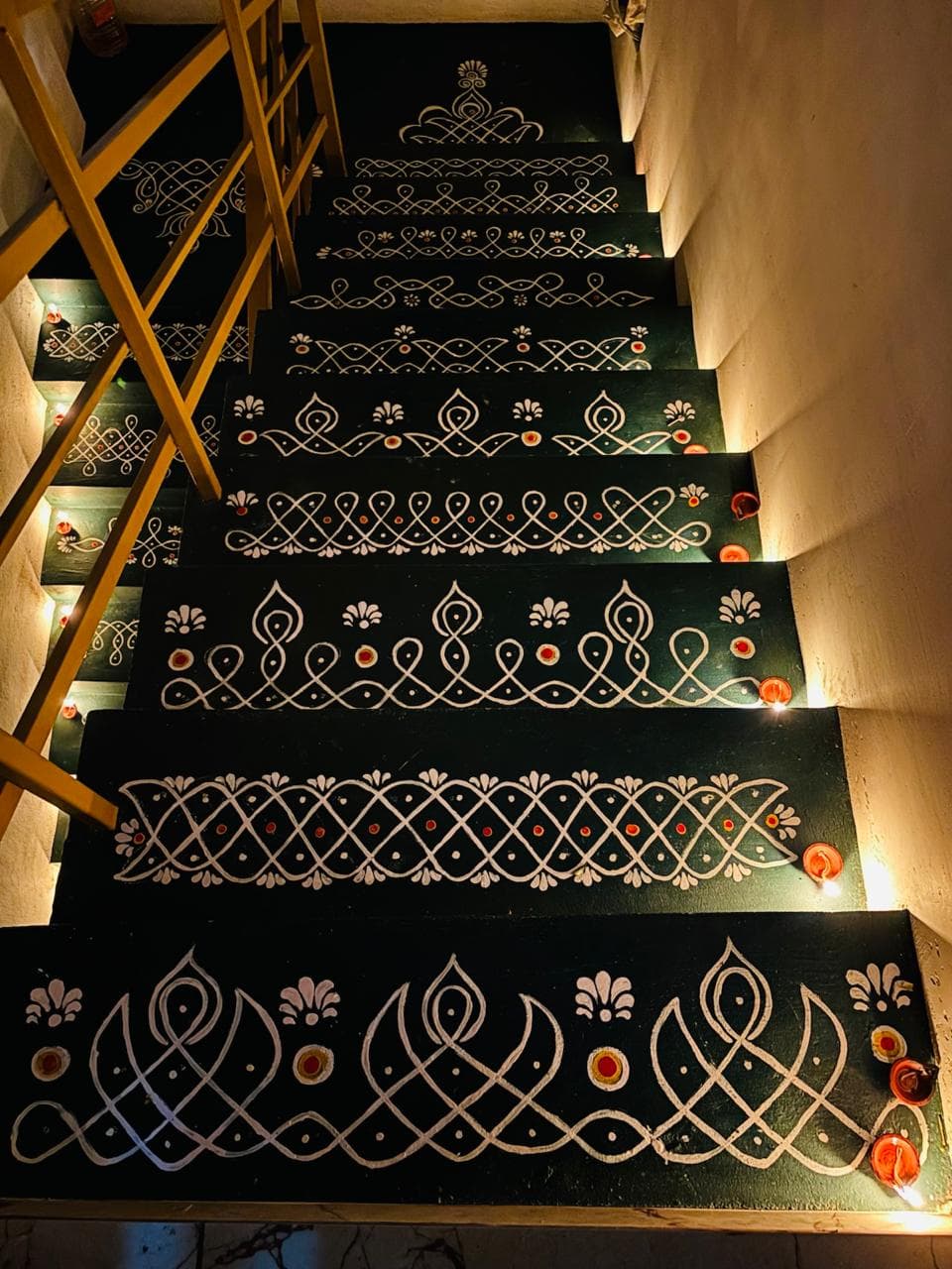 Green stairs decorated with white kolam patterns and lit diyas