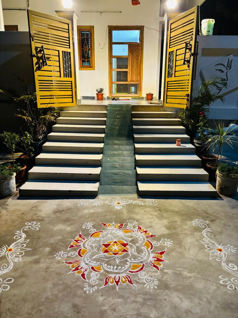 Night entrance with rangoli, yellow gates, and accessibility ramp